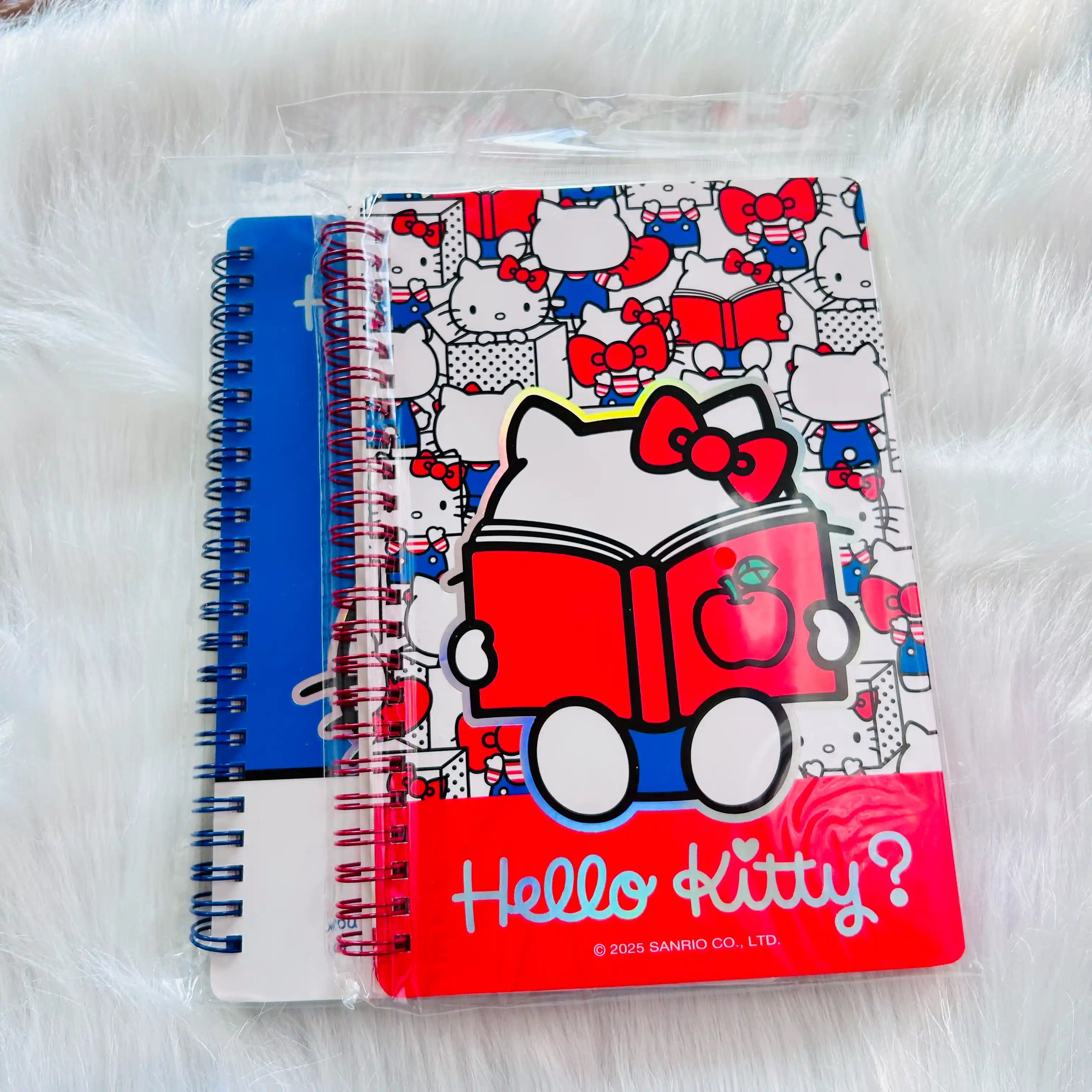 A Hello Kitty spiral notebook with a red and white patterned cover featuring a cartoon character reading a book, shown in its clear plastic packaging.