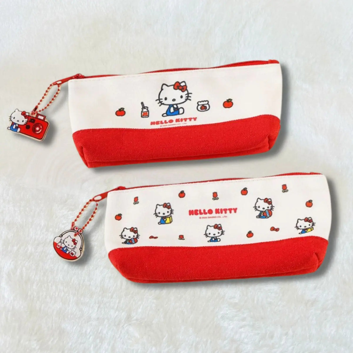 Two Hello Kitty zippered pencil cases on a soft white textured background. The top case is cream and red with a central Hello Kitty illustration, and the bottom case is cream and red with a scattered Hello Kitty pattern.