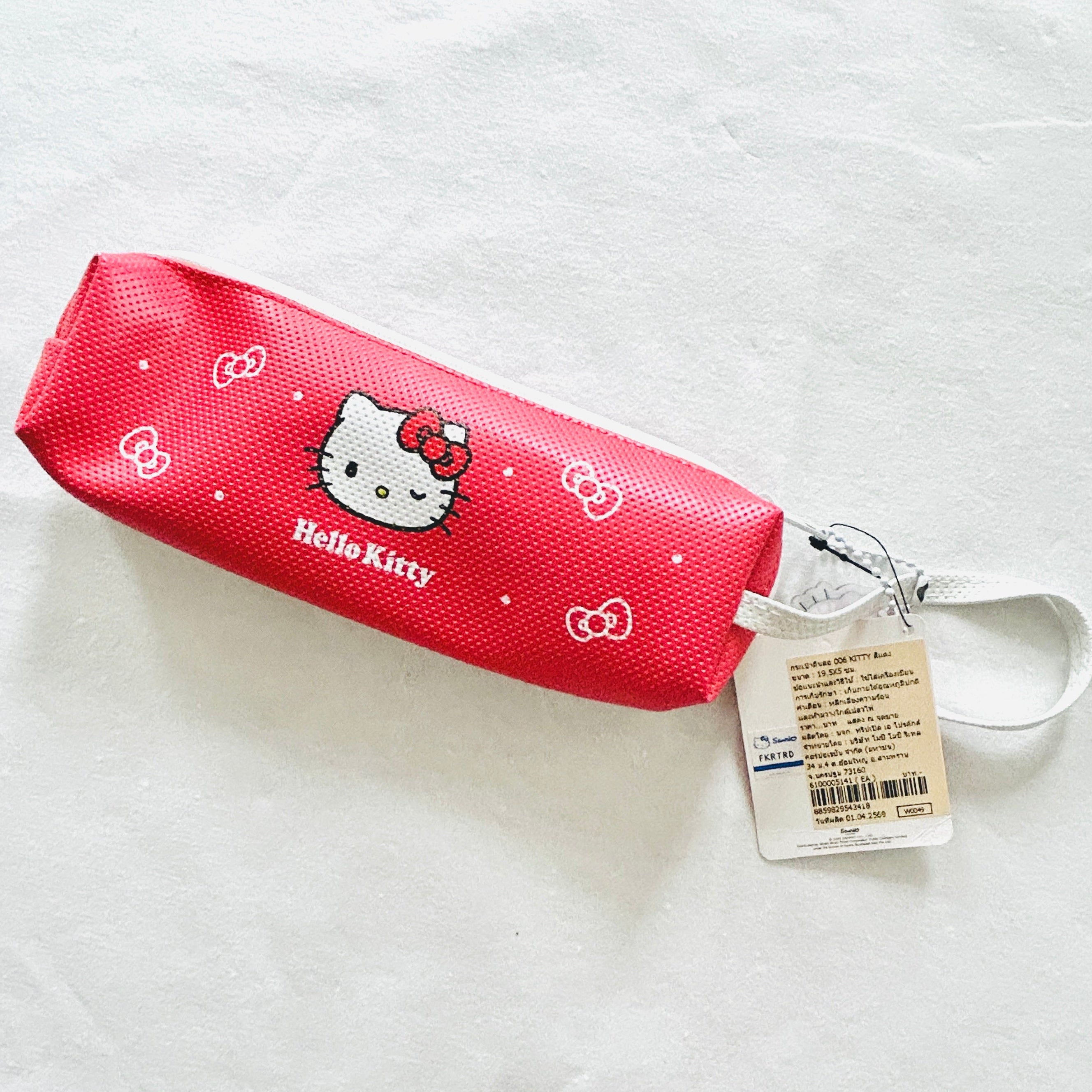 A red Hello Kitty pencil case with a white strap, featuring the Hello Kitty character and white bow patterns, with its original tag attached, on a white textured background.