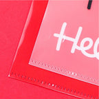 A close-up of a clear plastic sleeve or pocket with a white printed script lettering sample, placed over a bright red backing or card on a red background.