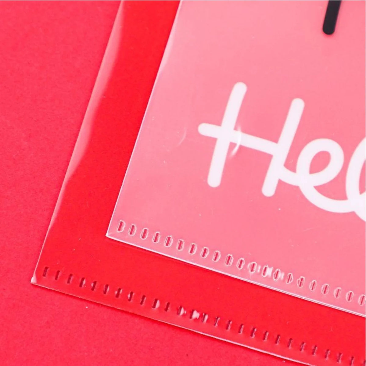 A close-up of a clear plastic sleeve or pocket with a white printed script lettering sample, placed over a bright red backing or card on a red background.