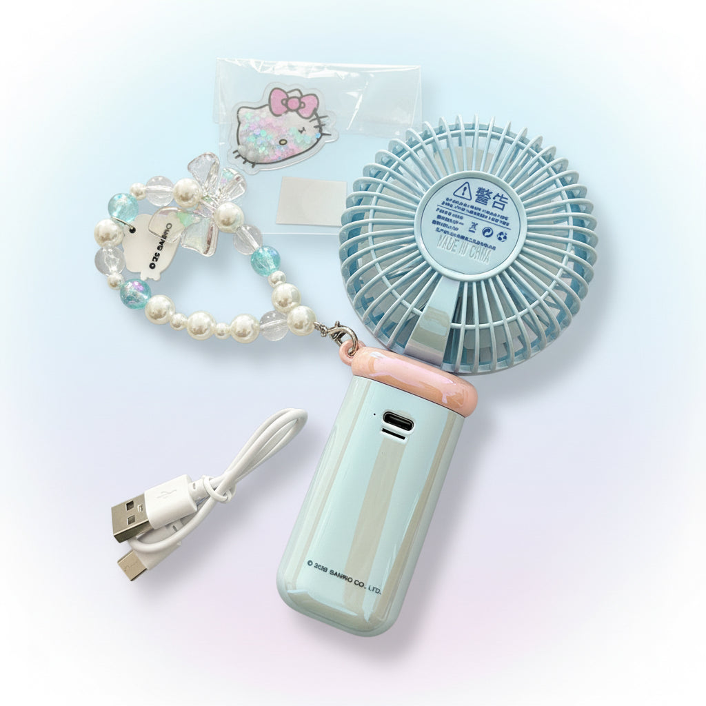 A light blue portable handheld fan with a pink accent on the handle, shown with a pearl-and-bead wrist strap, USB charging cable, and a small Hello Kitty sticker on a pale blue background.