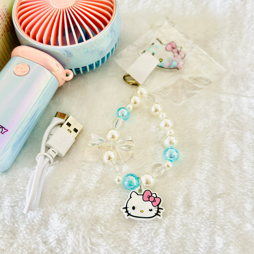 A close up view of the handheld fan's Hello Kitty beaded strap or charm, along with a USB charging cable and a small handheld fan nearby.  