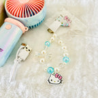 A close up view of the handheld fan's Hello Kitty beaded strap or charm, along with a USB charging cable and a small handheld fan nearby.  