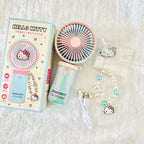 Hello Kitty portable handheld fan set with its retail box, pink and light blue fan, a wrist strap with a Hello Kitty charm, a USB charging cable.
