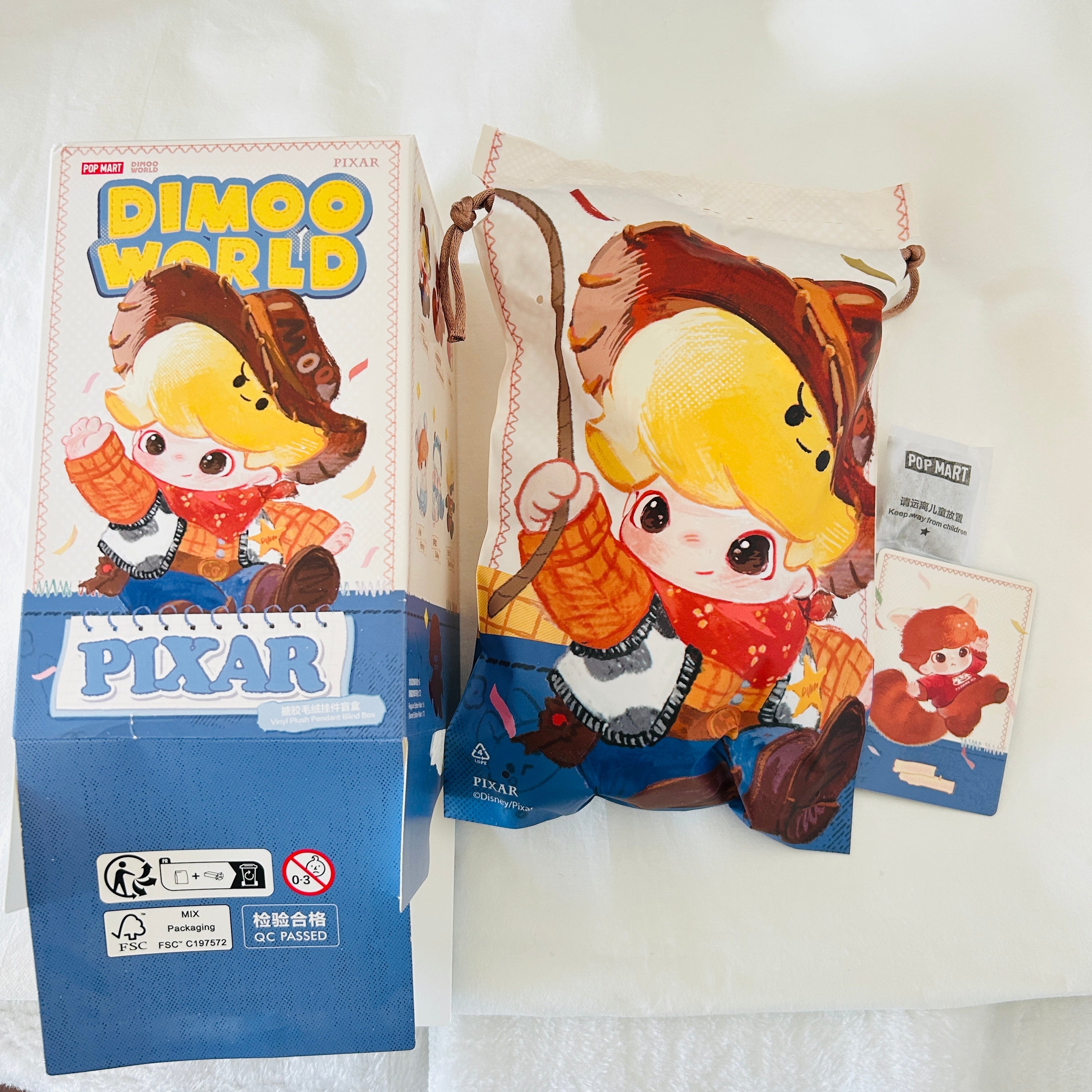 A Disney Pixar Dimoo World collectible figure plush pendant product box. Opened from the bottom and shows a card of Red Panda Mei.