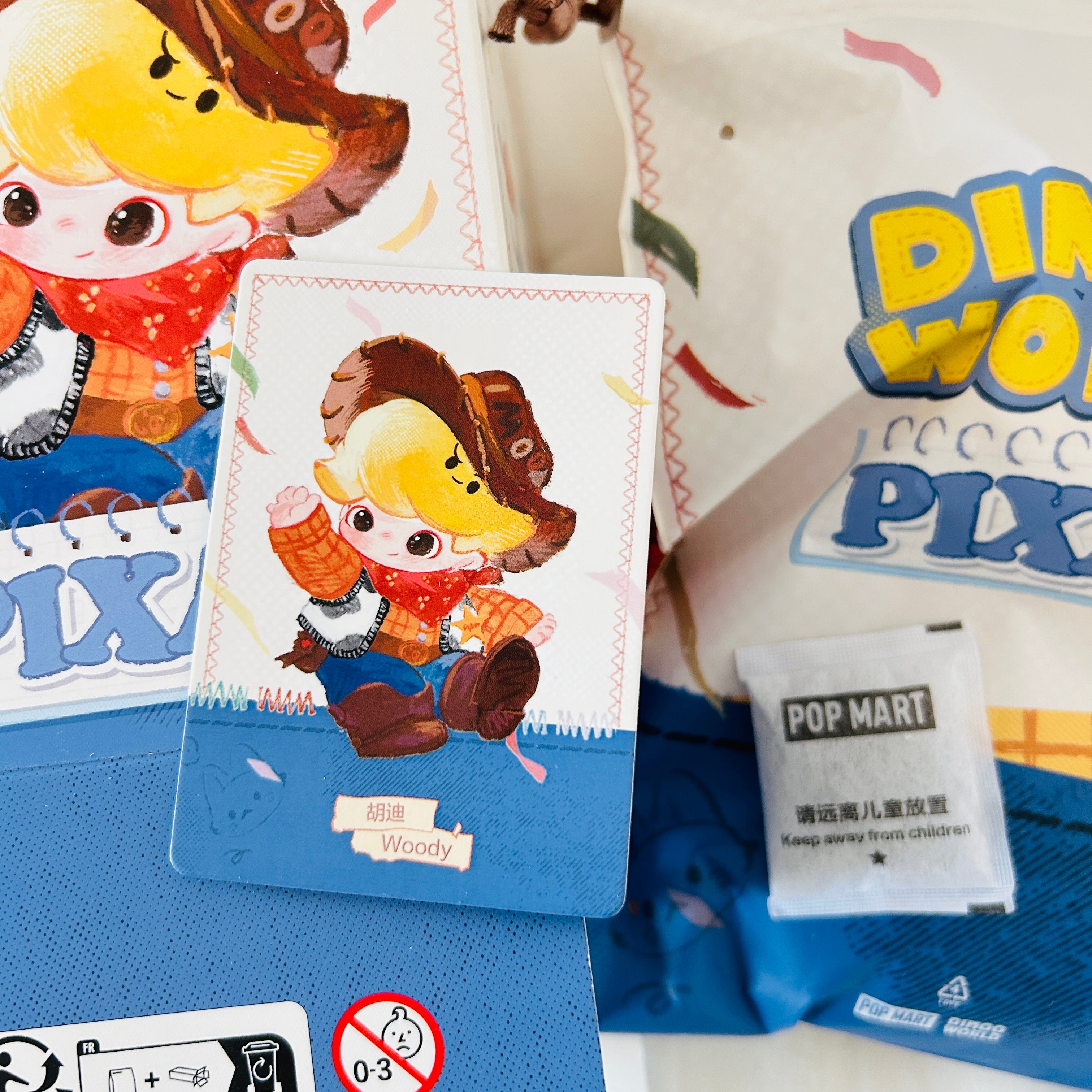 A Pop Mart collectible card featuring a cartoon Woody character, displayed alongside its packaging and a branded POP MART packet on a blue surface.