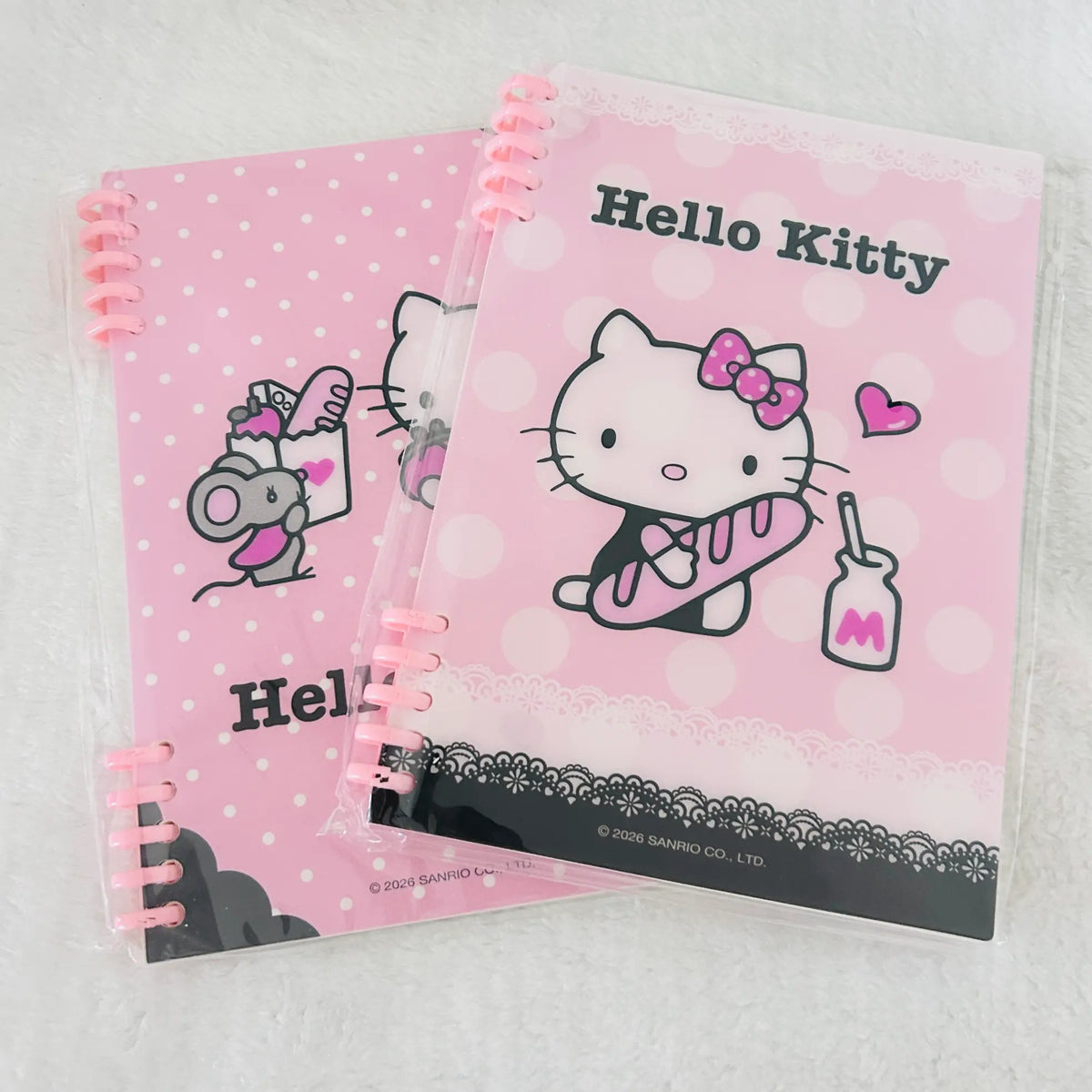 Two pink Hello Kitty spiral-bound notebooks with clear plastic covers, featuring Hello Kitty illustrations and pink polka dots on a white textured background.