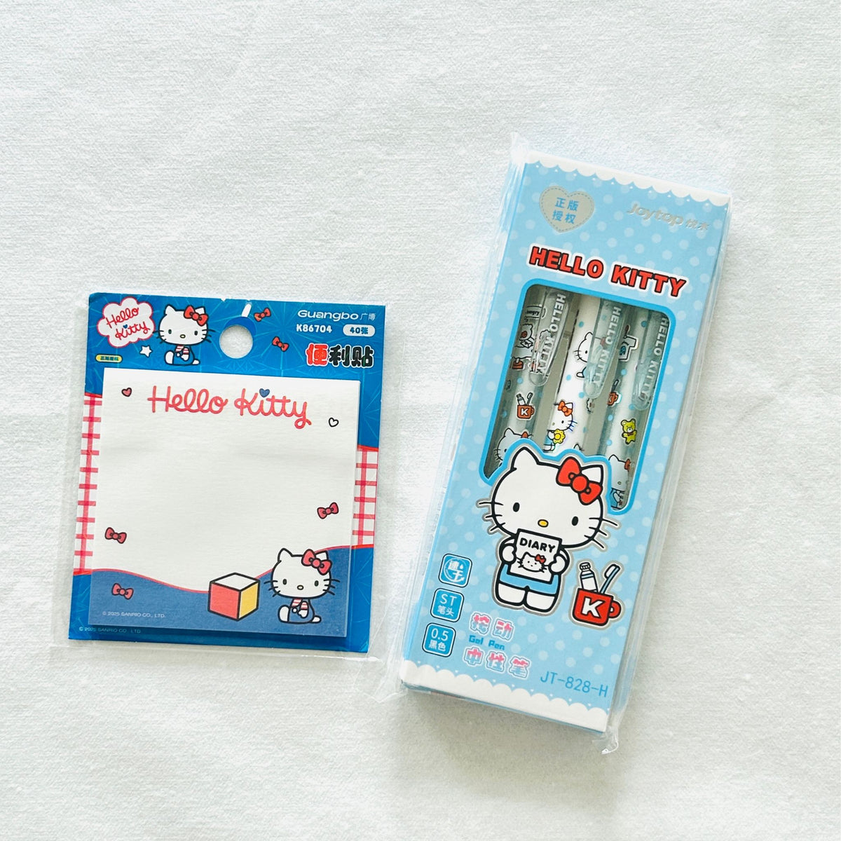 Hello Kitty stationery set featuring a blue notepad and three matching pens in a light blue package, displayed on a soft pastel background with heart and snowflake decorations.