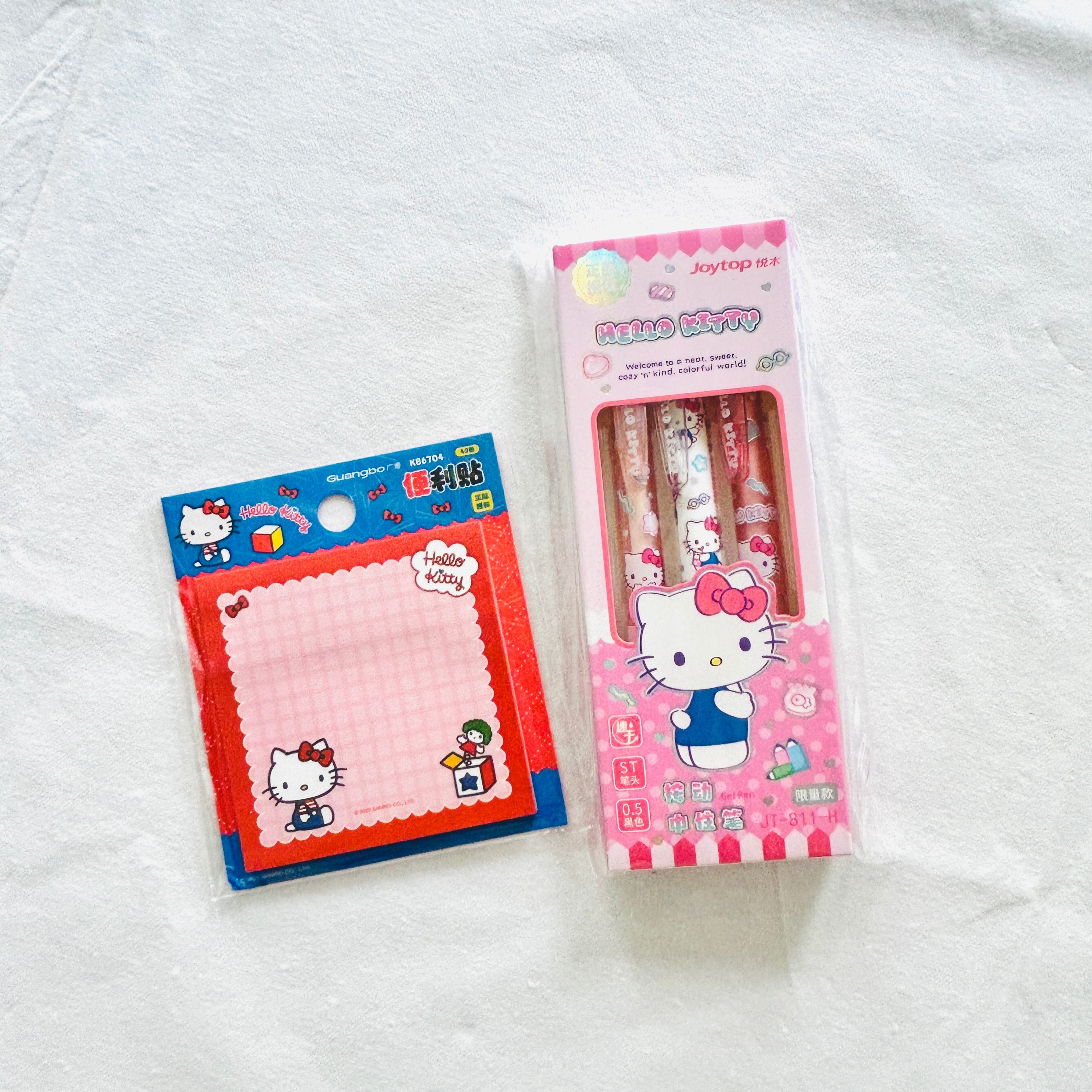 Hello Kitty stationery set including a pink notepad with a red border and a matching pink pen pack in clear plastic packaging, displayed on a white textured fabric background.