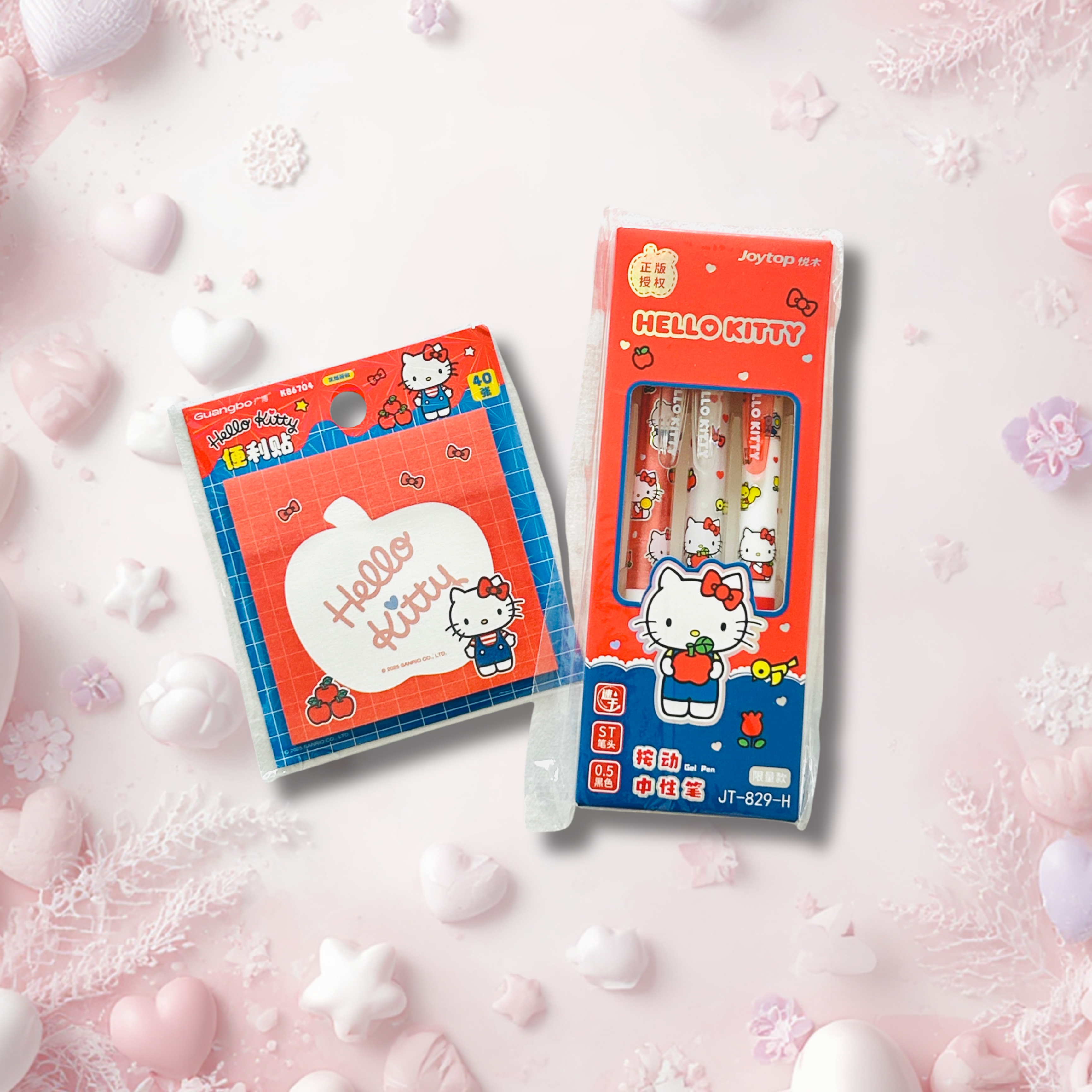 Hello Kitty stationery set featuring a pack of three pens in a clear window box and a matching notepad in a plastic sleeve, both decorated with Hello Kitty illustrations, set against a soft pink background with decorative hearts and snowflakes.