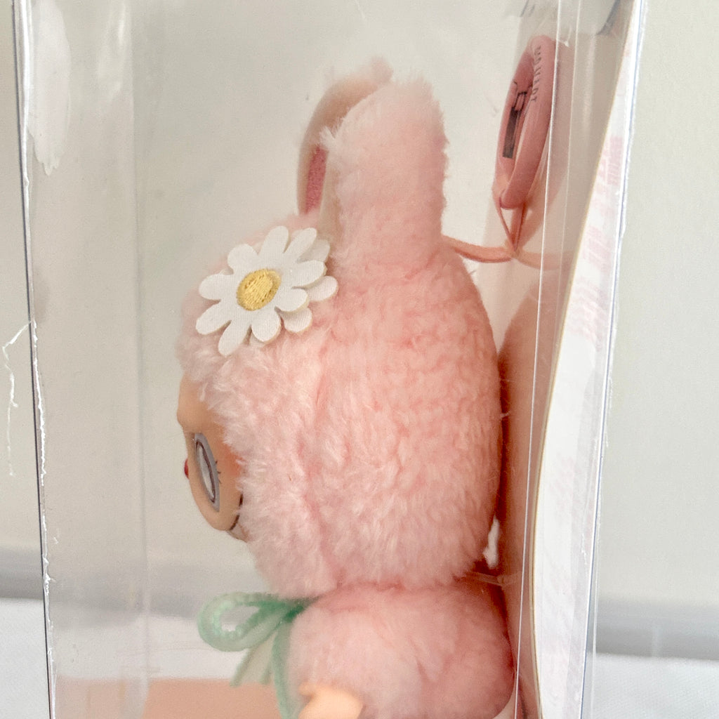 A Labubu Mokoko inside clear retail packaging, featuring a white daisy flower with a yellow center on its head and a small mint green bow at the neck.