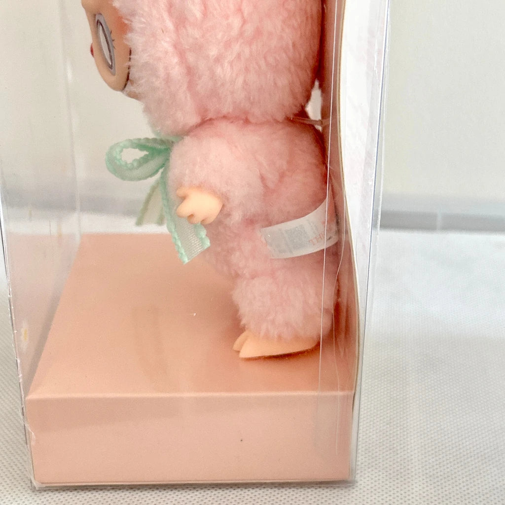A Mokoko Labubu with fluffy pink fur, peach-colored limbs, and a mint green ribbon bow, displayed inside a clear plastic box with a pale pink base.
