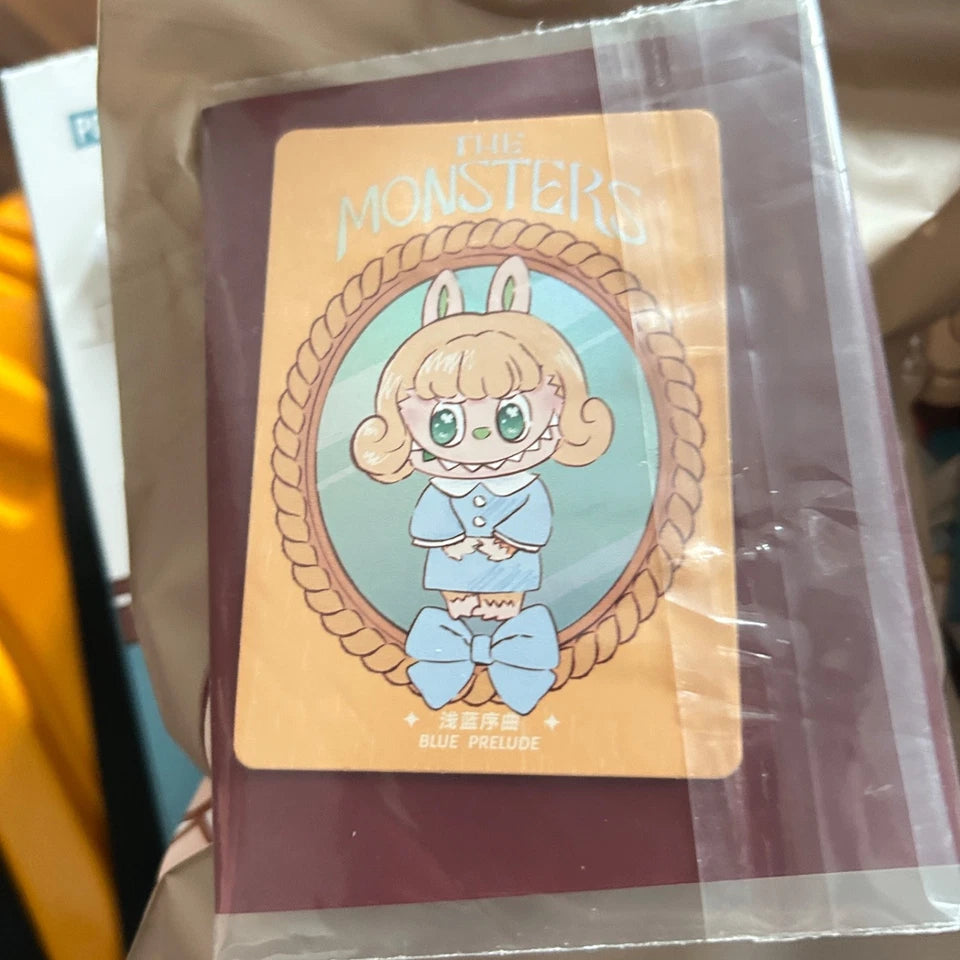 A packaged collectible card is labeled 'THE MONSTERS' at the top and 'BLUE PRELUDE' at the bottom, and it is sealed in clear plastic packaging.