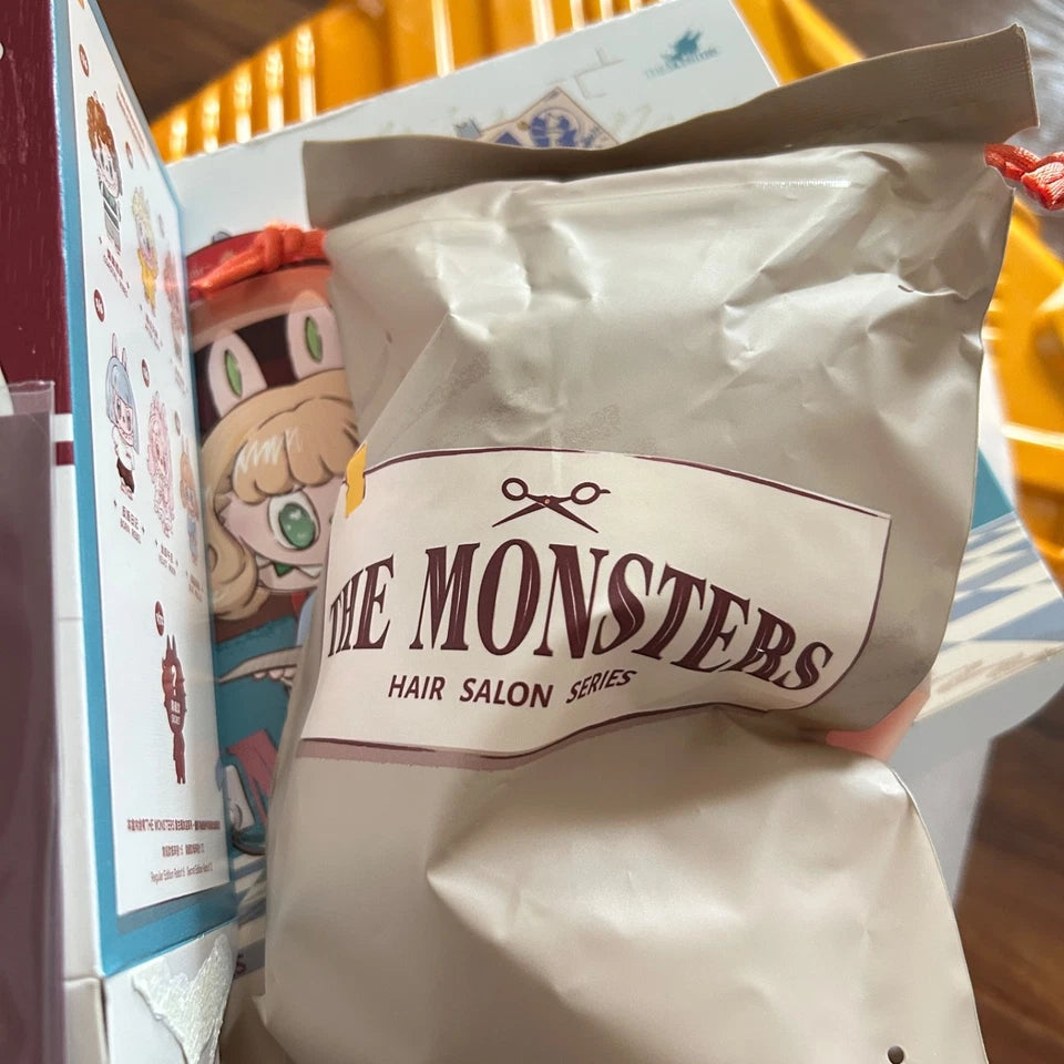 A close-up of a silver foil bag labeled 'THE MONSTERS HAIR SALON SERIES' with scissors icon, held in front of illustrated packaging boxes.