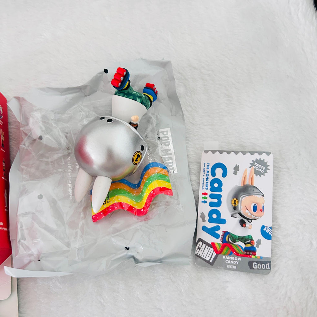 A Popdits Candy Rainbow Cave Shark figure in its clear plastic packaging, shown next to its illustrated card packaging on a white faux fur surface.