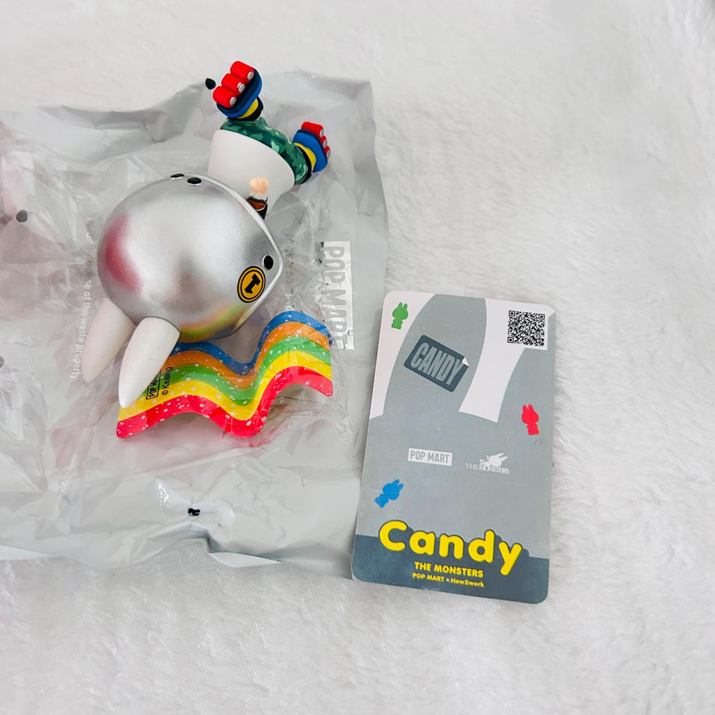 A collectible toy figure of Candy the Monster from Pop Mart, still in its clear plastic blister packaging, displayed next to its grey and yellow cardboard card on a white textured background.