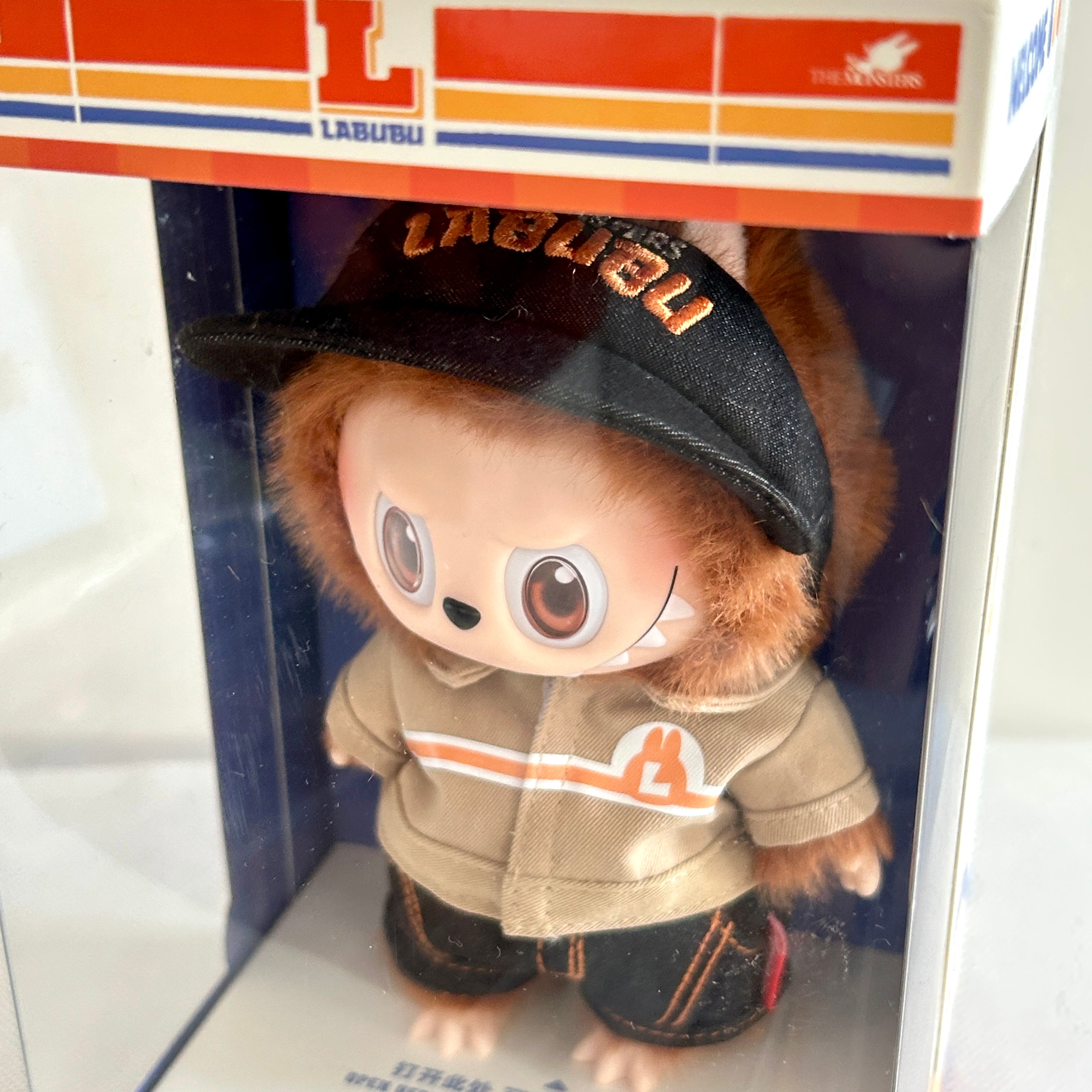A close-up front view of the side of a Labubu Wacky Mart Series plush doll, which with brown fur and wearing uniform. 