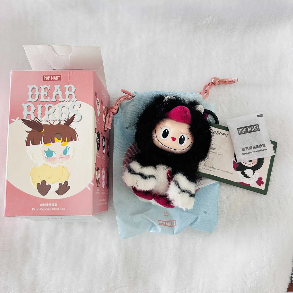 A Pop Mart 'Dear Birds' blind box mystery plush keychain set, showing the pink illustrated retail box, the black-and-white striped fuzzy bird plush. 