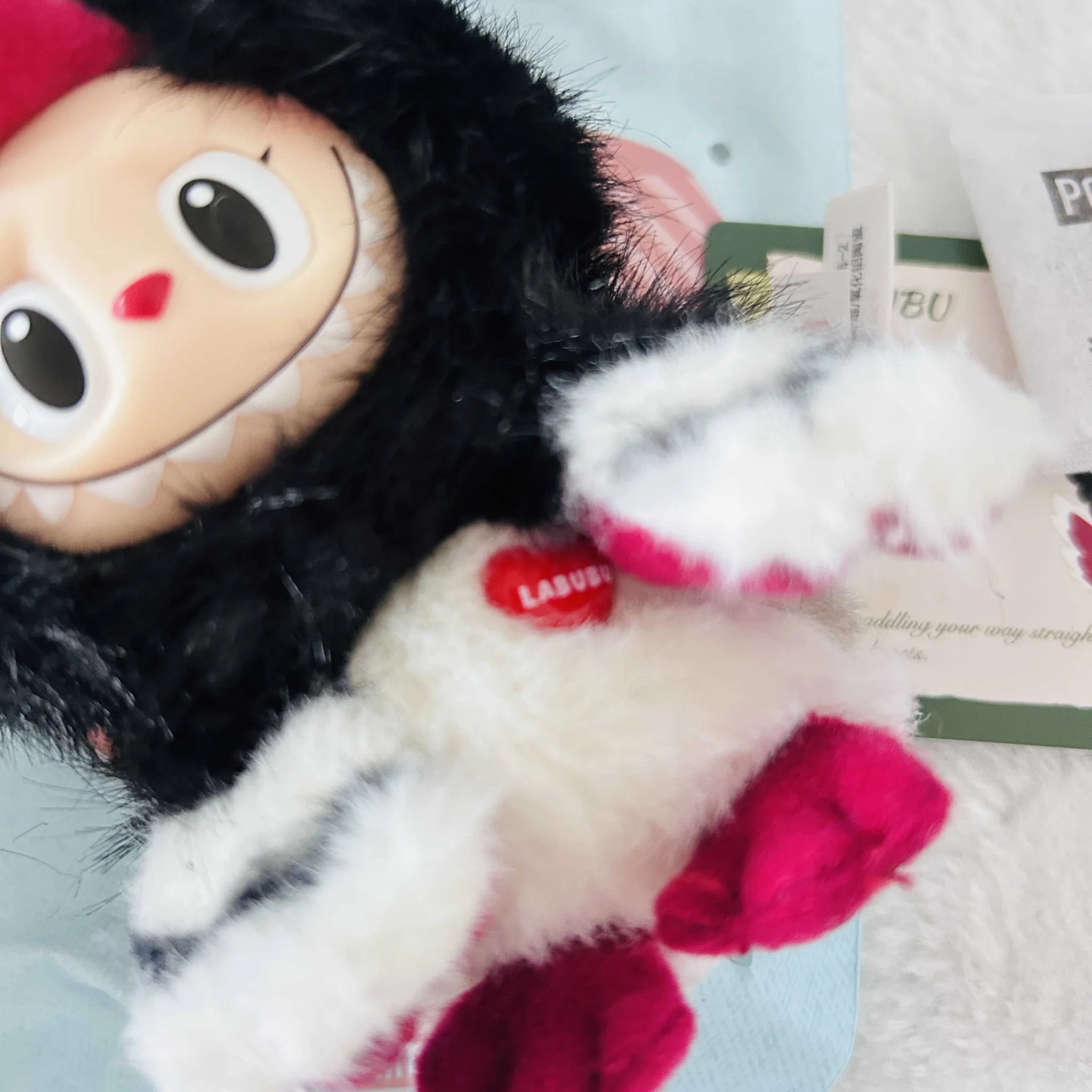 A close-up of a Labubu Dive Into Love plush toy with a black furry head, white body.