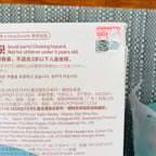 A close-up of a printed product label or packaging insert showing text, a QR code, and a small red warning seal, photographed on a gray textured surface.