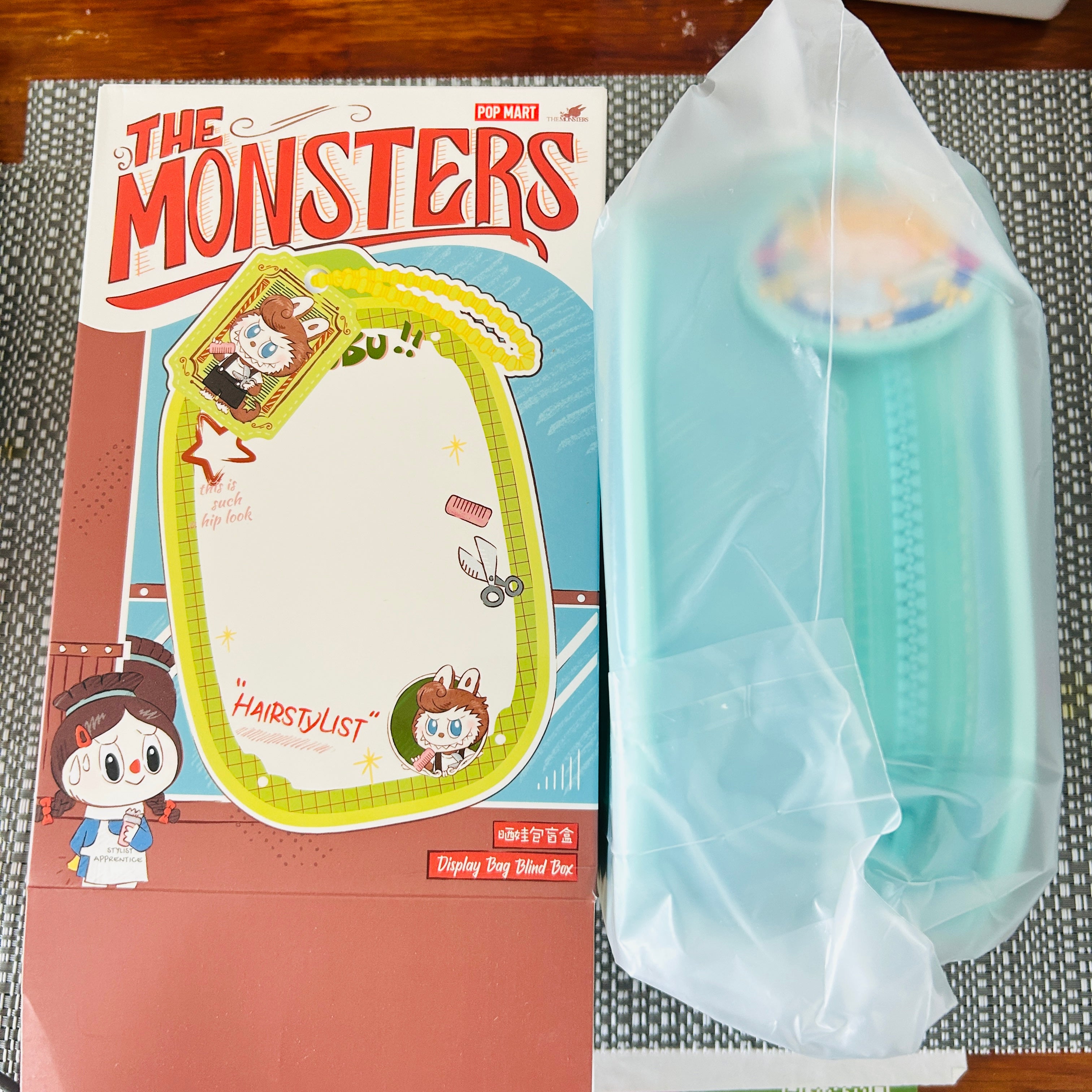 A boxed hair display pin set labeled 'The Monsters' shown next to its light blue plastic-wrapped package on a patterned mat.