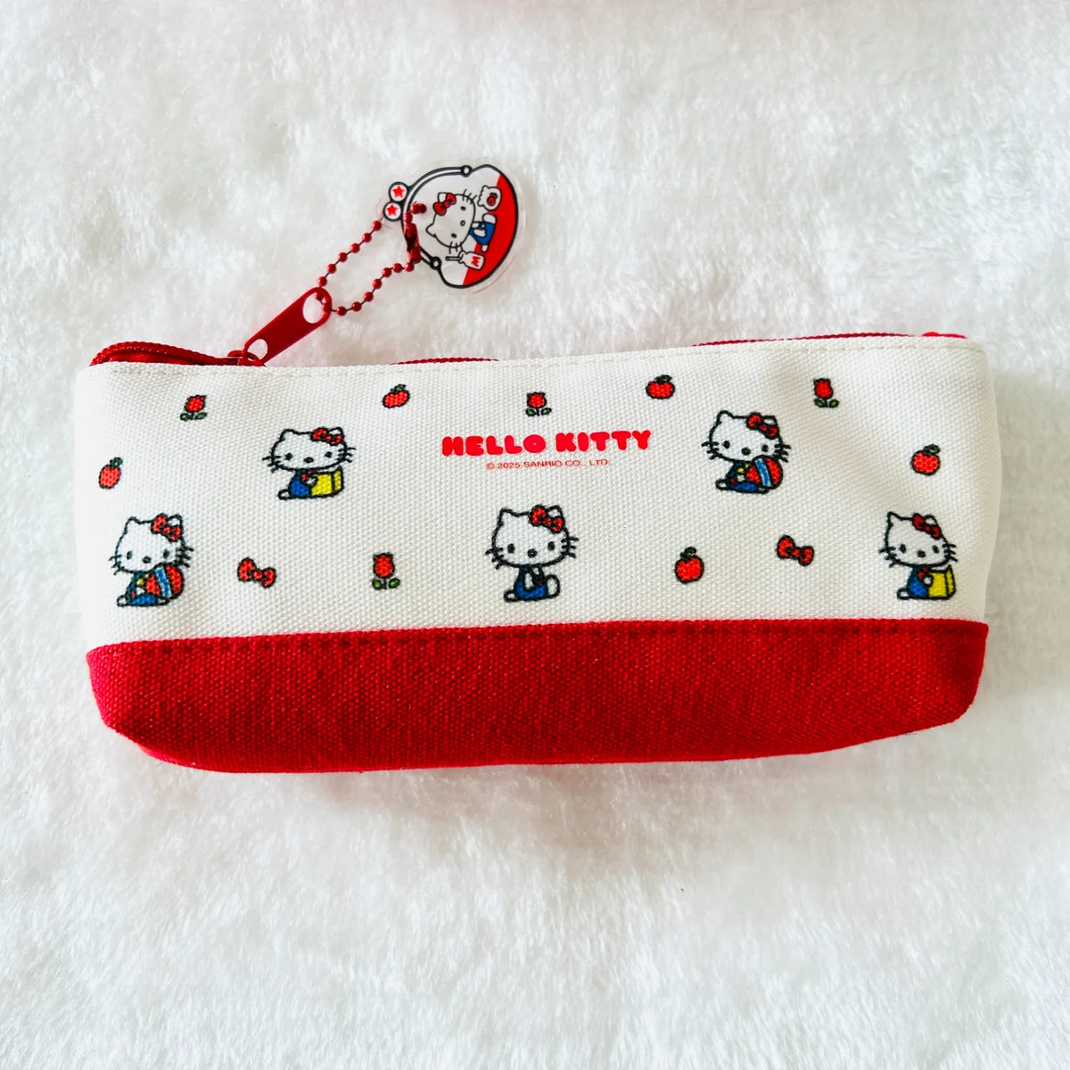 A Hello Kitty canvas pouch with a red bottom panel and a red zipper pull featuring Hello Kitty illustrations, placed on a white textured background.
