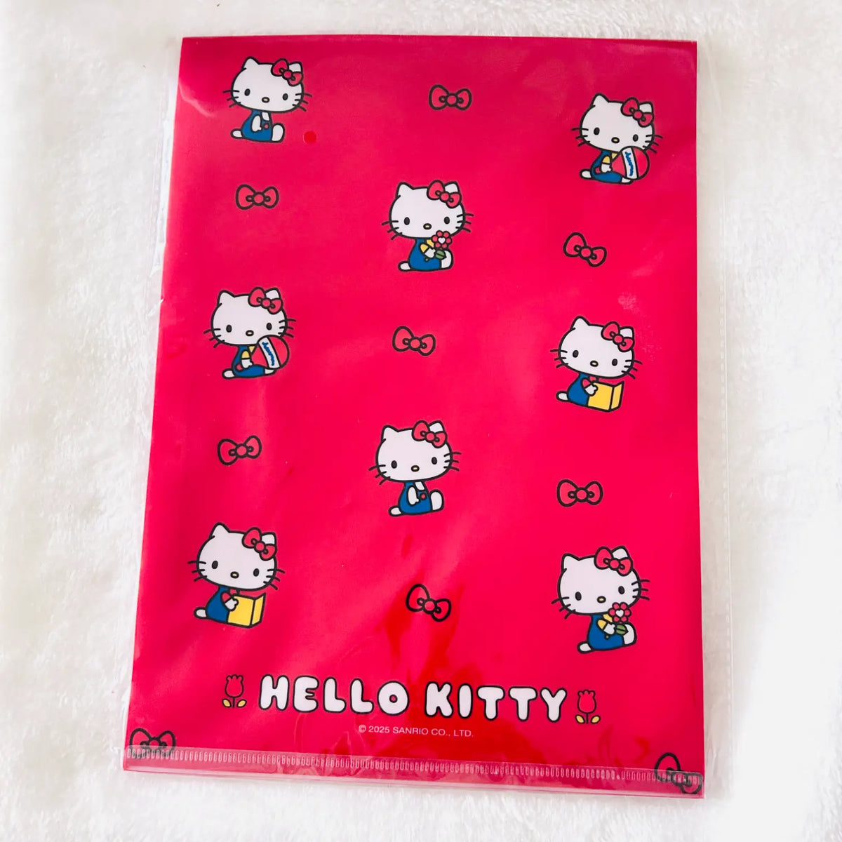A bright pink Hello Kitty file folder with a glossy finish, featuring printed illustrations of Hello Kitty in blue and yellow outfits, bows, and the 'HELLO KITTY' logo at the bottom.