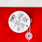 A round white product tag with printed text and barcode attached to a red item, with a clear plastic grommet and white string. The tag shows the brand name 'Simplicity' and 'Made in China' text.