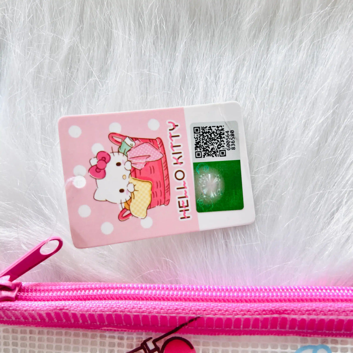 A pink Hello Kitty zip pouch. The product features a Hello Kitty picnic illustration and a green reflective sticker on the front.