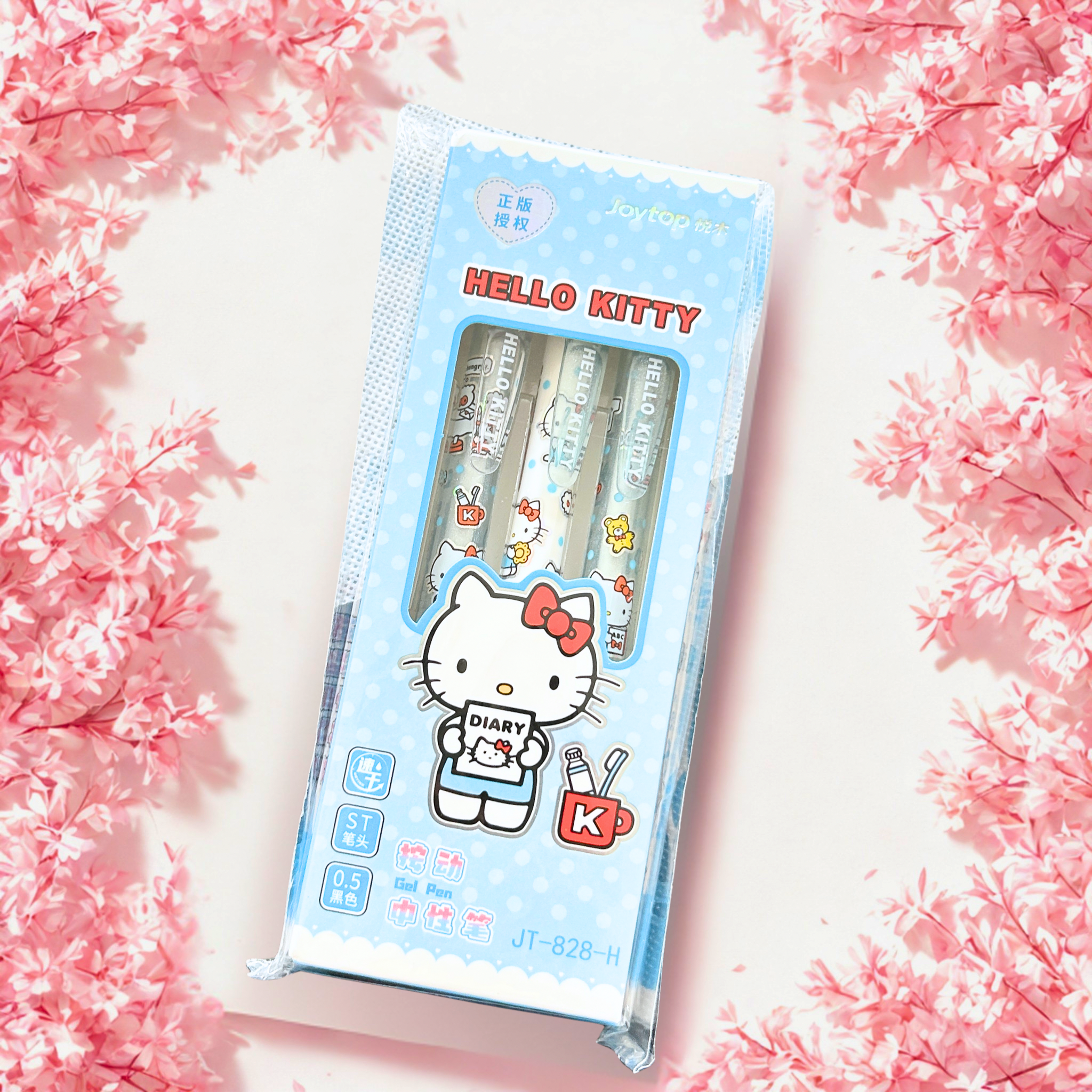 A boxed set of three Hello Kitty pens by Jaytop, displayed on a white surface surrounded by pink cherry blossoms. The packaging is predominantly pink with a large Hello Kitty illustration and a clear window showing the pastel-colored pens inside.