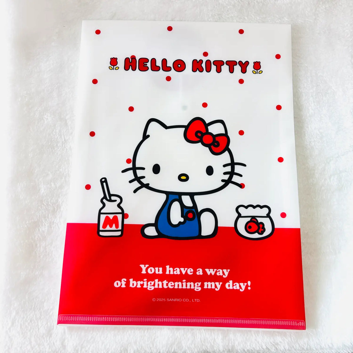 A Hello Kitty printed file folder or document holder. The folder is white with red polka dots, a red Hello Kitty bow, a red bottom band, and a cartoon illustration of Hello Kitty in blue overalls holding a small jar.