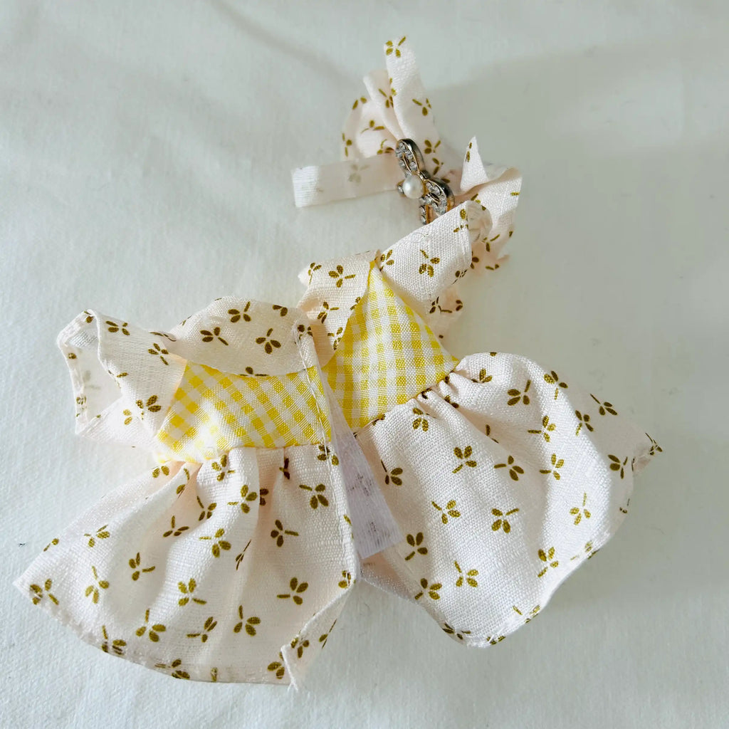 A back view of a  plush doll dress in yellow colour and floral pattern, with a matching bow. 