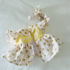 A back view of a  plush doll dress in yellow colour and floral pattern, with a matching bow. 