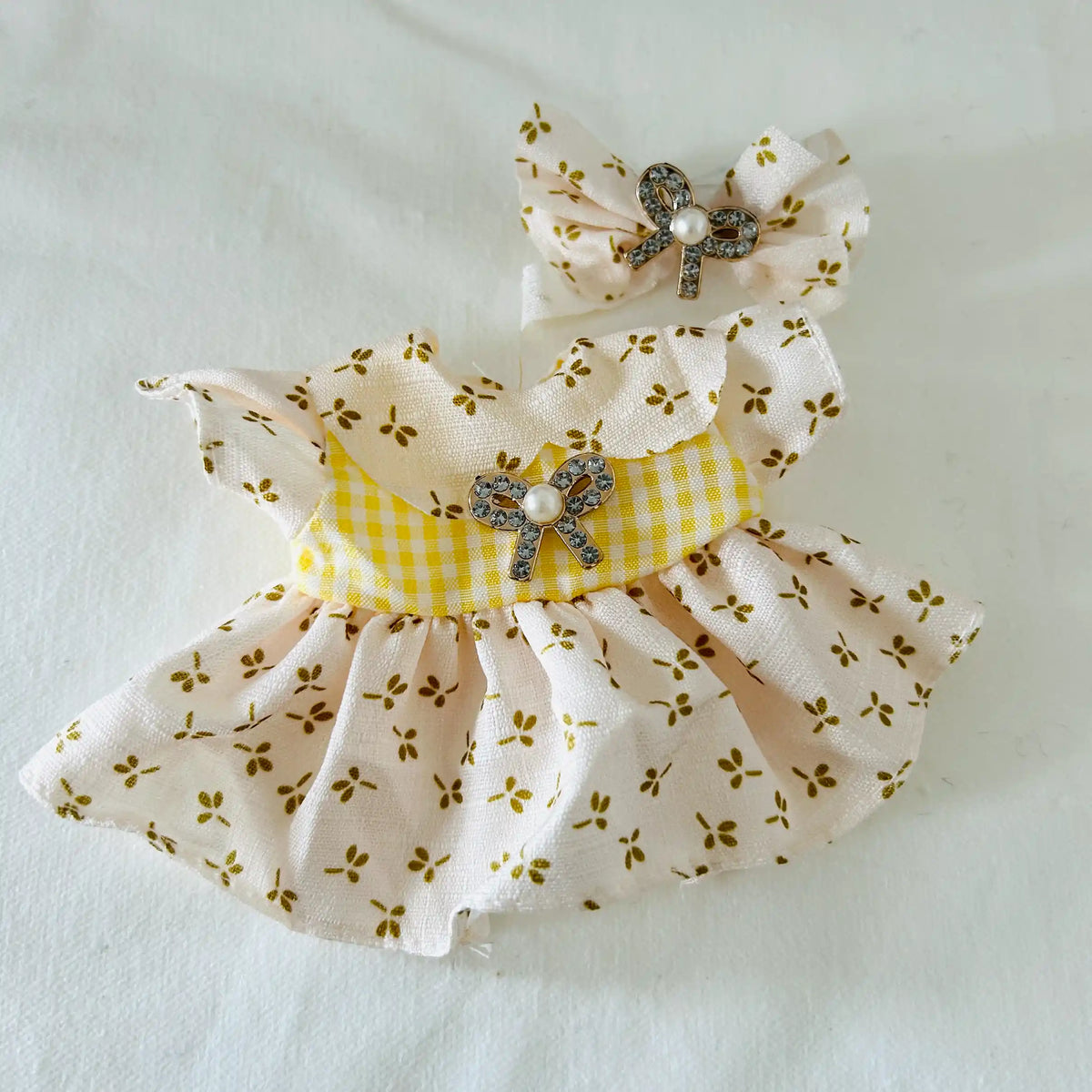 A Labubu doll yellow floral dress with white gingham bodice, and a matching bow headband with a rhinestone bow and pearl.