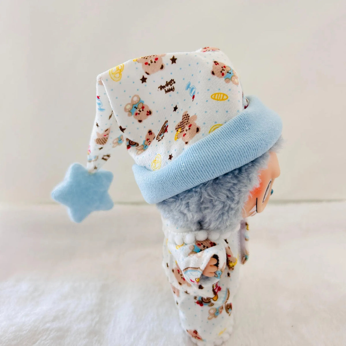 A Labubu doll wearing a white patterned pyjamas set with a light blue cuff and a matching light blue star-shaped hat.