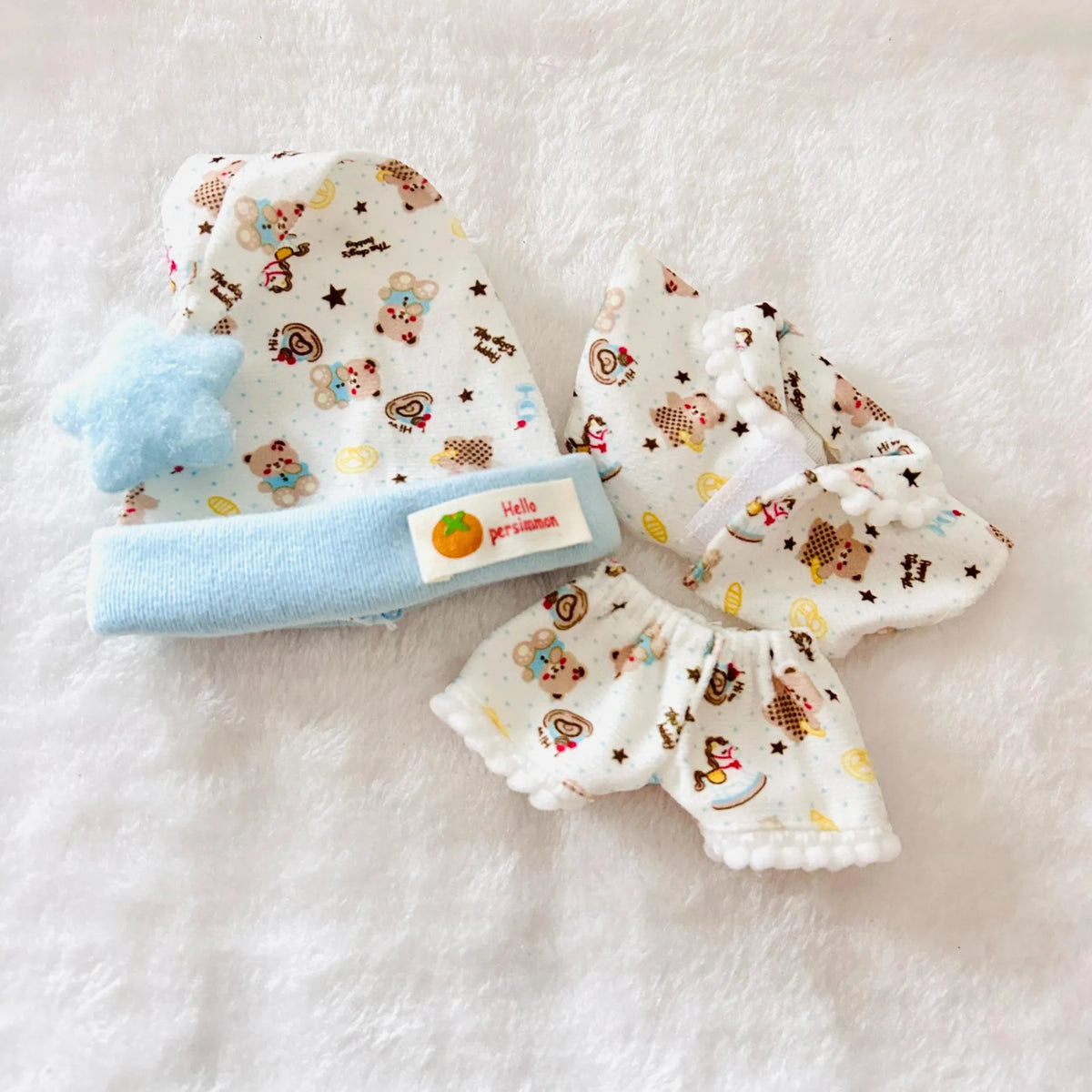 A Labubu doll pyjamas set including a top and pants with bears patterned, with a light blue hat.