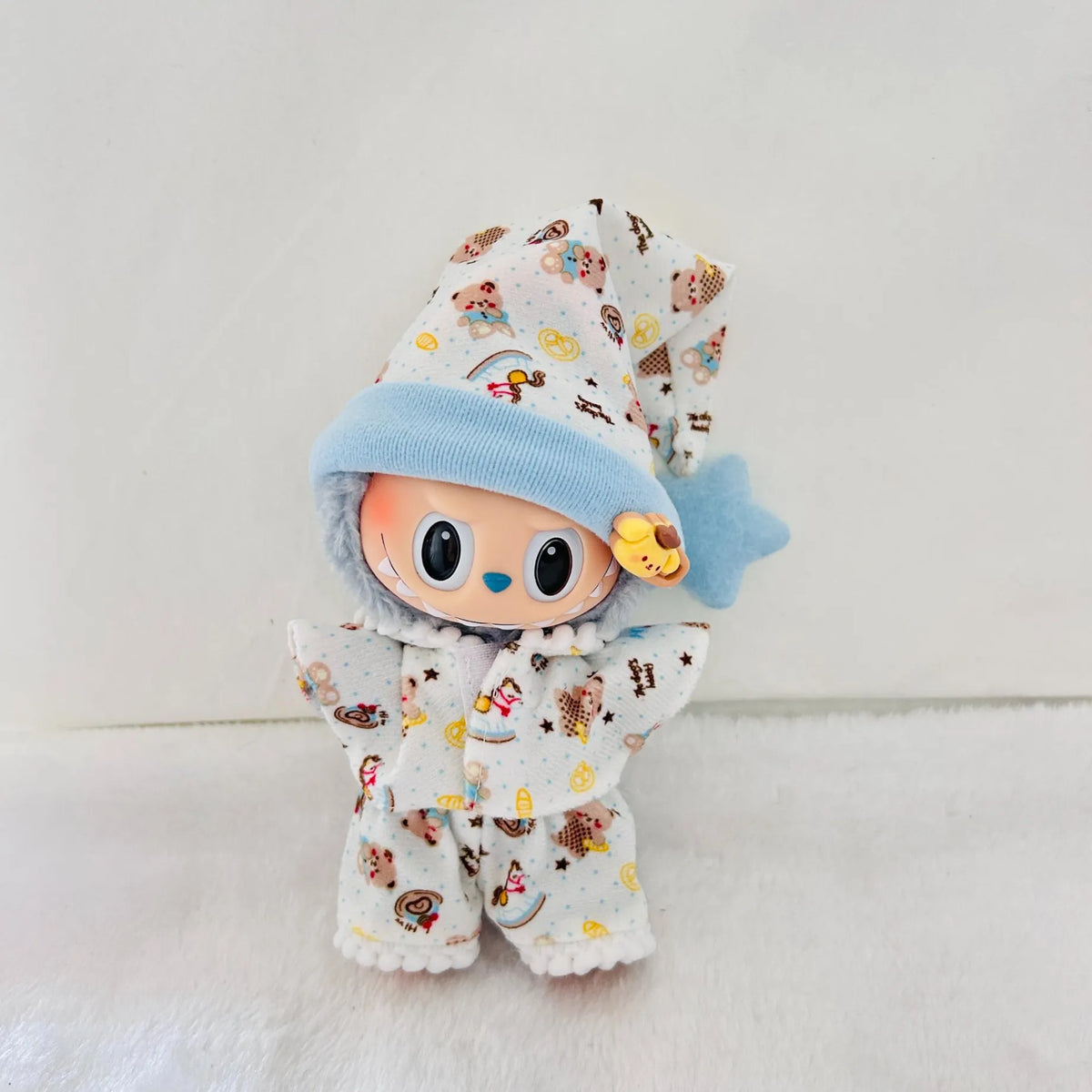 A small plush doll or collectible figure wearing a white pyjama set with a colourful cartoon animal print and a light blue hood.