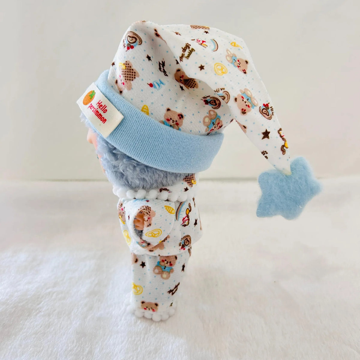 A Labubu doll dressed in a white patterned outfit with teddy bear prints, a light blue knit hat, and a blue star accessory.