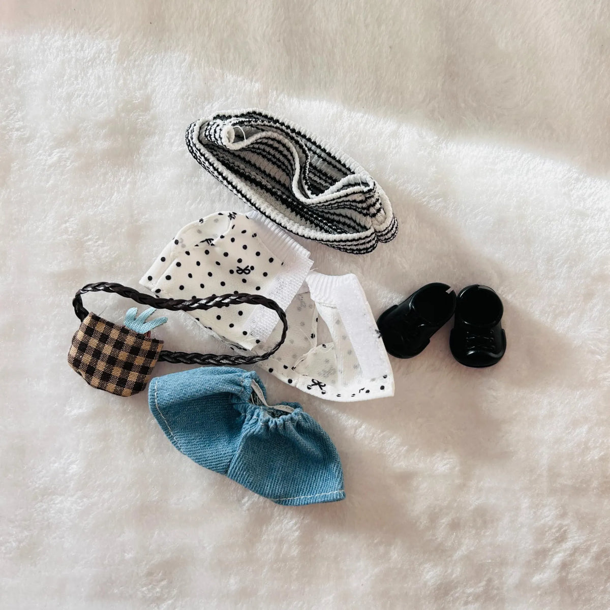 A back view of a Labubu doll outfit, including a black and white striped tee, a blue knit bootie, a plaid and white polka dot bonnet, and a pair of black shoes.