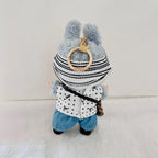 A back view of a Labubu wearing black and white striped knit hat, a white polka-dot vest, and blue denim pants.