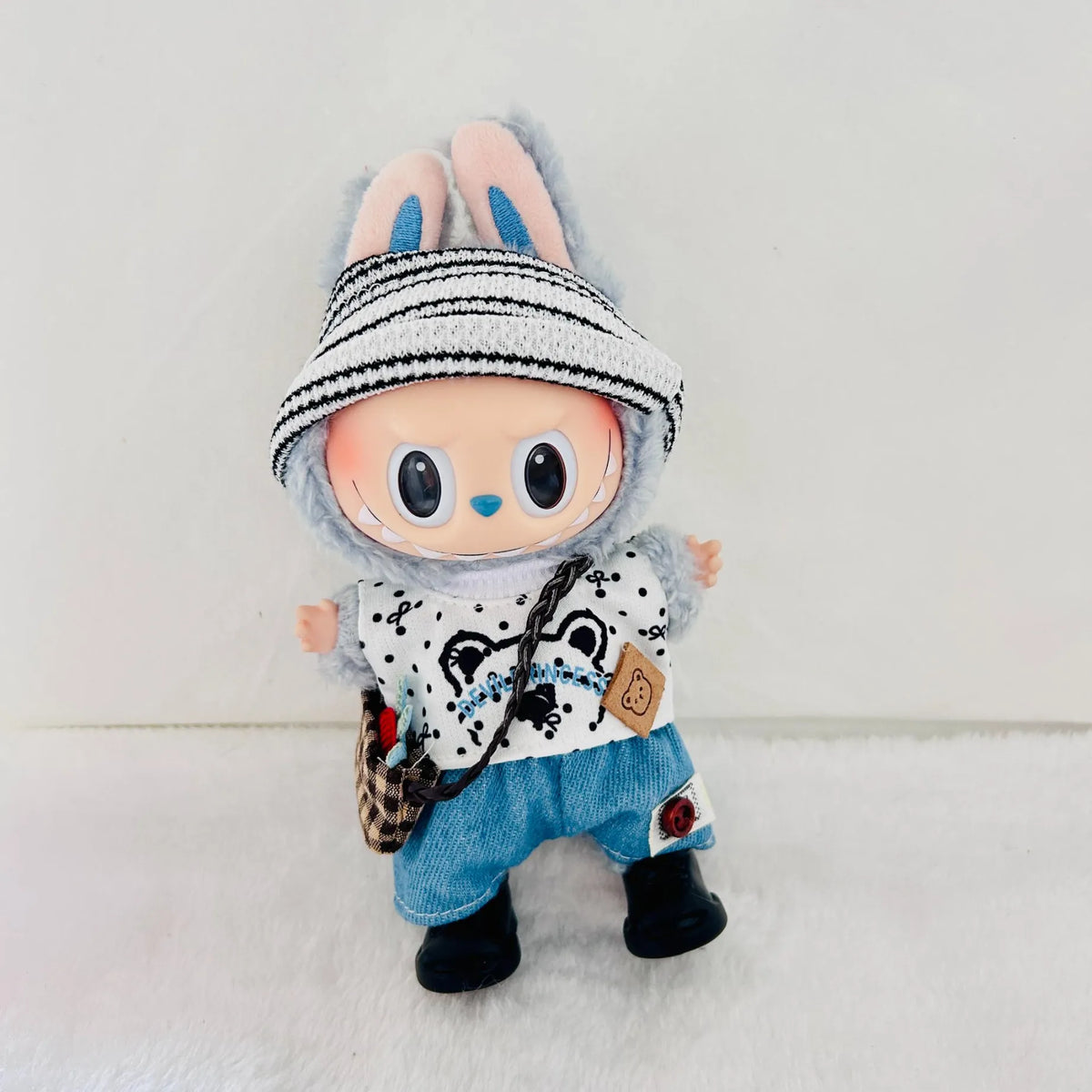 A Labubu doll with a black-and-white striped headband, wearing a white patterned top, blue denim shorts, and black boots.