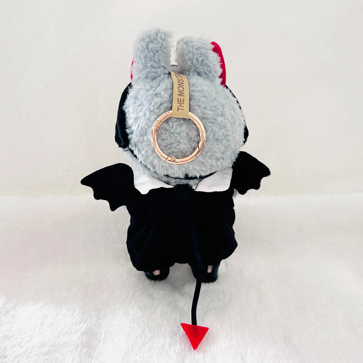 A back view of Labubu wearing a black  devil costume with bat wings, a red tail tip.