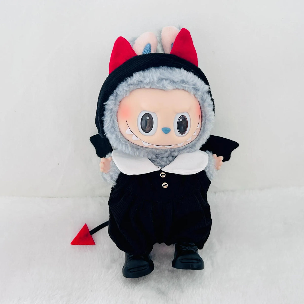 A Labubu vinyl plush doll dressed in a black devil costume with white collar, red devil horns, and a small red tail.