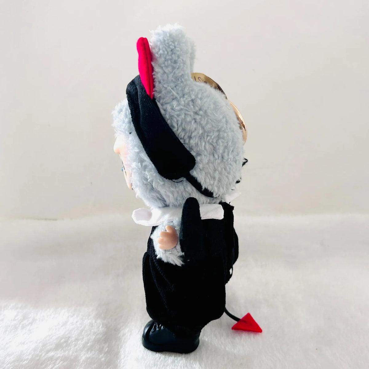 A Labubu plush toy wearing a black outfit and hat with small red horns, standing against a plain light background.