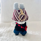 A back view of a Labubu plush wearing a burgundy and white striped hat, a black and white top, blue shorts.