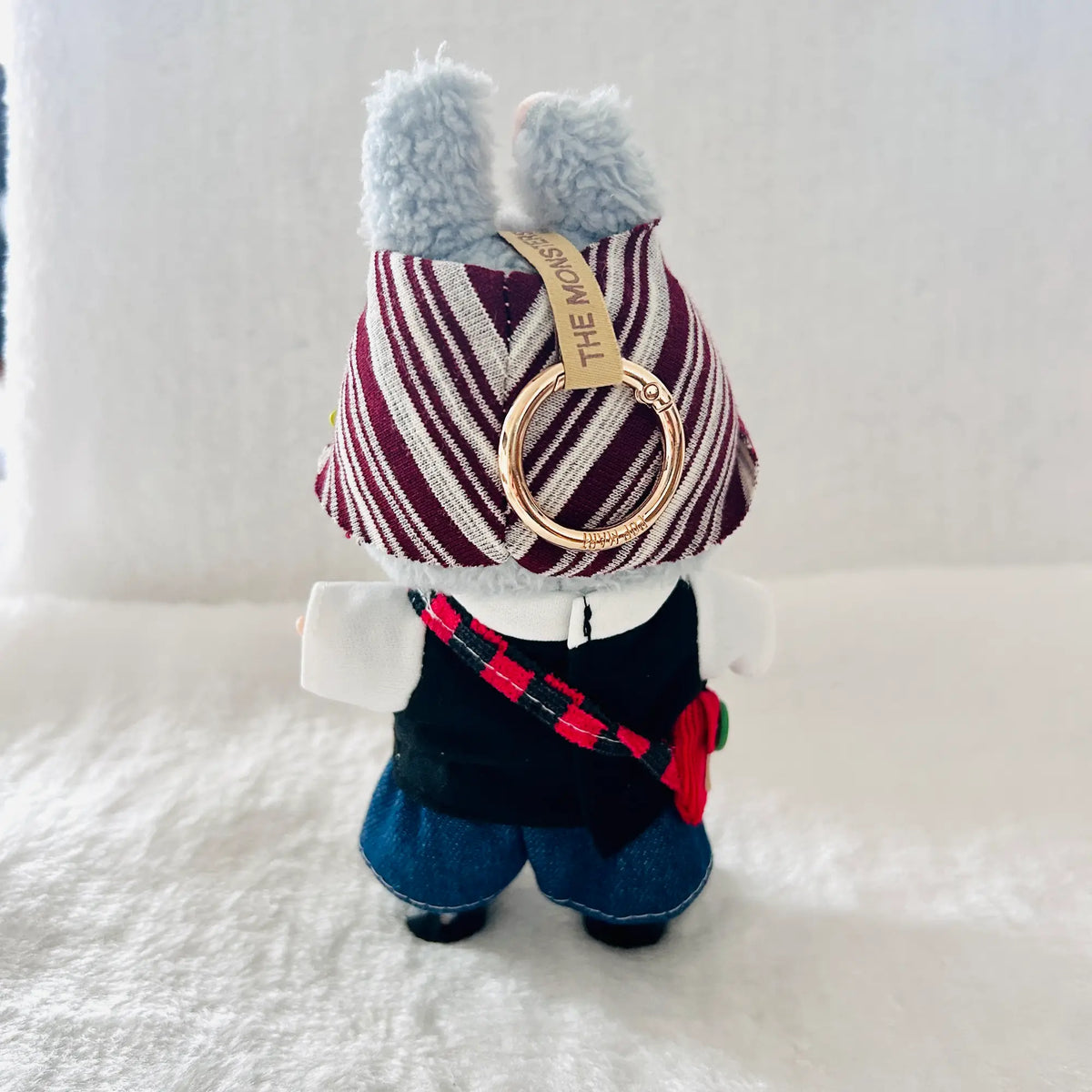 A back view of a Labubu plush wearing a burgundy and white striped hat, a black and white top, blue shorts.