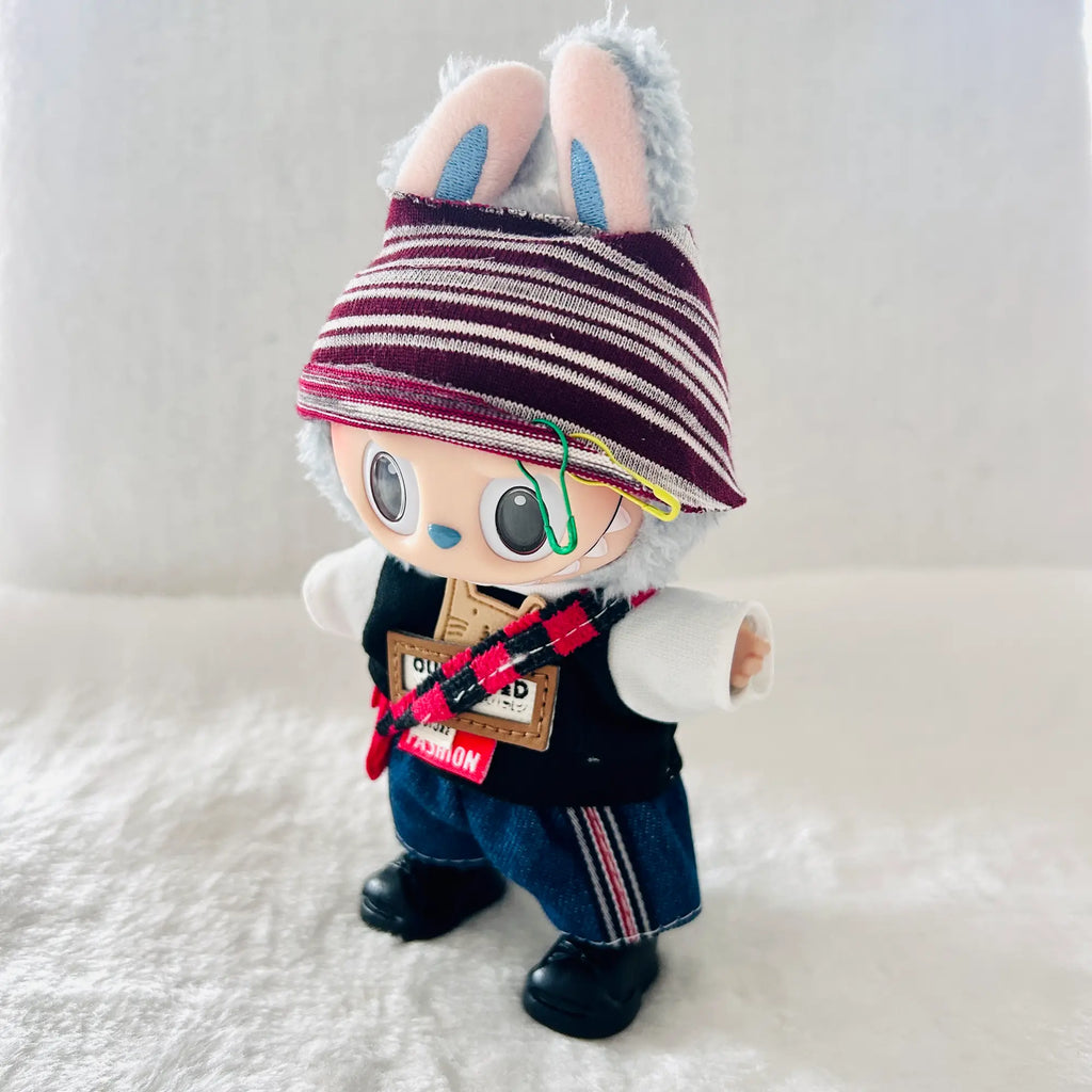 A custom handcrafted plush doll wearing a burgundy and white striped beanie, a black vest, blue jeans, and black shoes. 