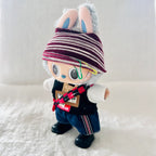 A custom handcrafted plush doll wearing a burgundy and white striped beanie, a black vest, blue jeans, and black shoes. 