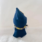 Back view of a Labubu wearing a a dark blue cape, with a plaid collar in yellow, gray, and purple, and white fluffy pom-poms on the sides.